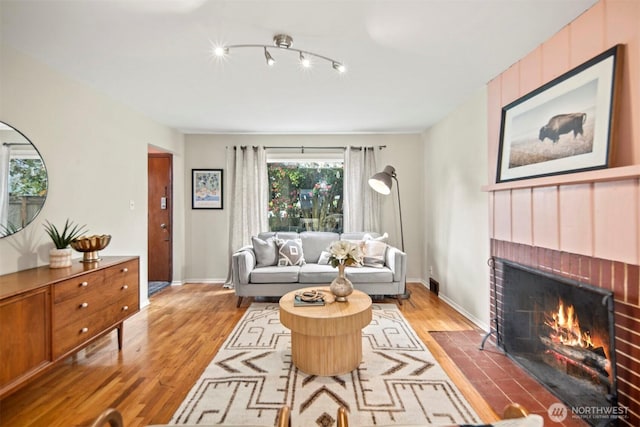 living area featuring baseboards, a brick fireplace, and wood finished floors