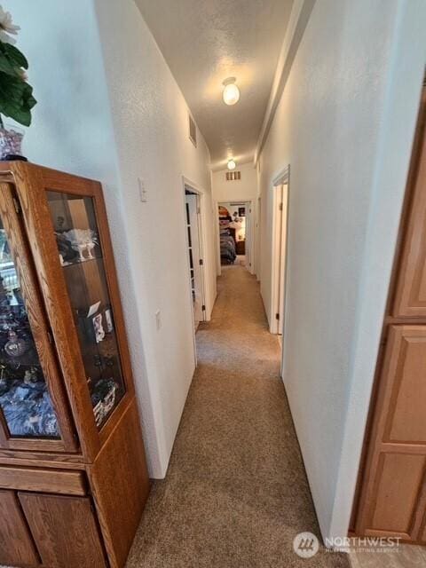 hall featuring a textured wall, visible vents, and light carpet