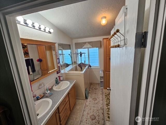 full bath featuring double vanity, a textured ceiling, lofted ceiling, and a sink