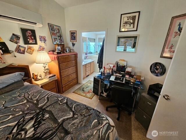 bedroom with light colored carpet, a wall mounted air conditioner, and connected bathroom