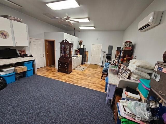 interior space featuring a wall mounted air conditioner, light wood-type flooring, light carpet, and ceiling fan