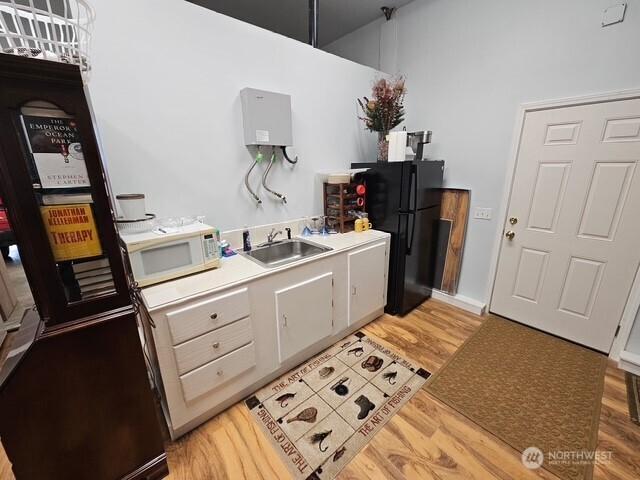 kitchen with white microwave, light wood-type flooring, freestanding refrigerator, and a sink