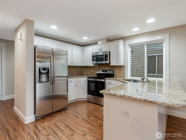 kitchen with a peninsula, light wood-style floors, appliances with stainless steel finishes, and a sink