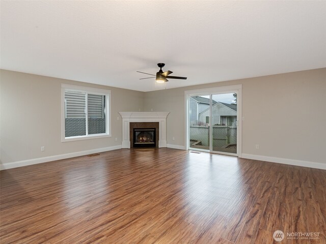 unfurnished living room with a glass covered fireplace, wood finished floors, baseboards, and a ceiling fan