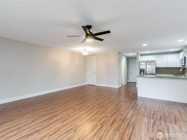 unfurnished living room with light wood-type flooring, a ceiling fan, a sink, recessed lighting, and baseboards