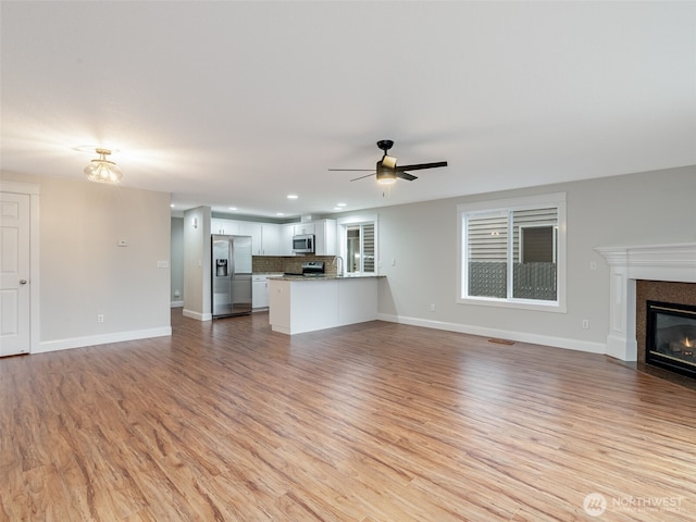 unfurnished living room with a fireplace with flush hearth, light wood-style flooring, baseboards, and ceiling fan