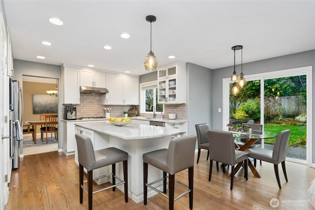 kitchen featuring glass insert cabinets, under cabinet range hood, a breakfast bar, stainless steel appliances, and white cabinetry