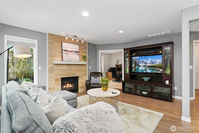 living room with wood finished floors, baseboards, visible vents, recessed lighting, and a tile fireplace