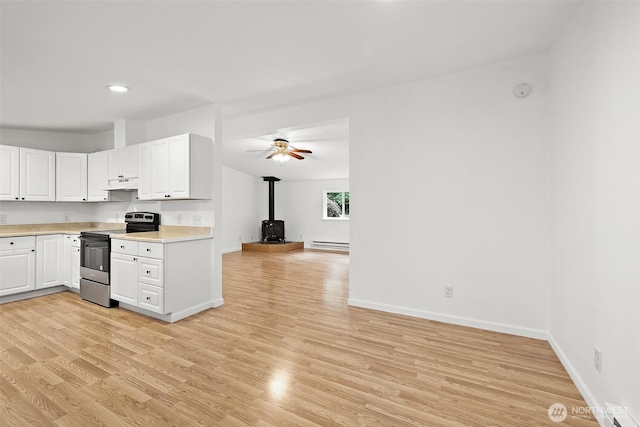 kitchen featuring a wood stove, light countertops, electric stove, under cabinet range hood, and a baseboard heating unit