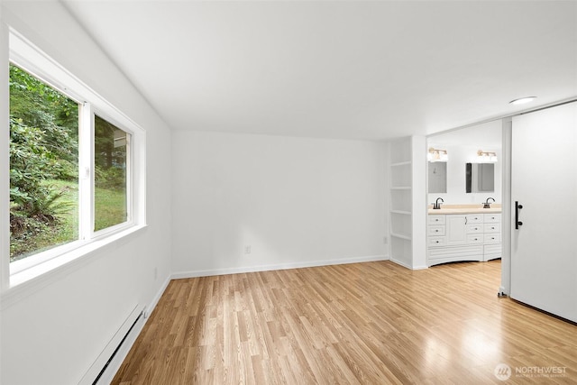 spare room featuring a sink, a baseboard heating unit, baseboards, and light wood-style floors