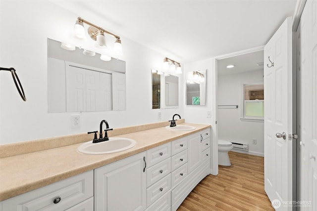 bathroom with a baseboard heating unit, double vanity, toilet, and a sink