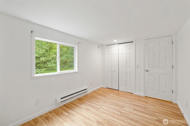 unfurnished bedroom with a baseboard heating unit, baseboards, light wood-style floors, and a closet