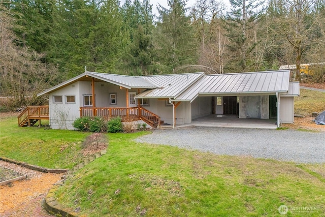 view of front of property with gravel driveway, a carport, a front lawn, and metal roof