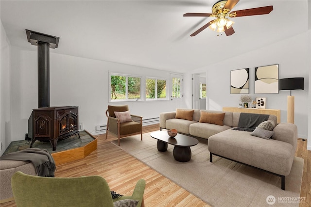 living room with a baseboard heating unit, vaulted ceiling, a wood stove, wood finished floors, and a ceiling fan