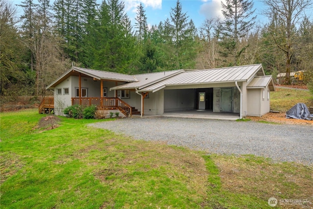 view of front of house with a standing seam roof, gravel driveway, a front yard, metal roof, and a carport