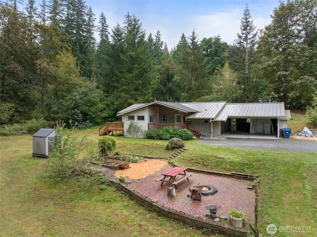 view of front of house featuring a standing seam roof, a fire pit, gravel driveway, an outdoor structure, and metal roof