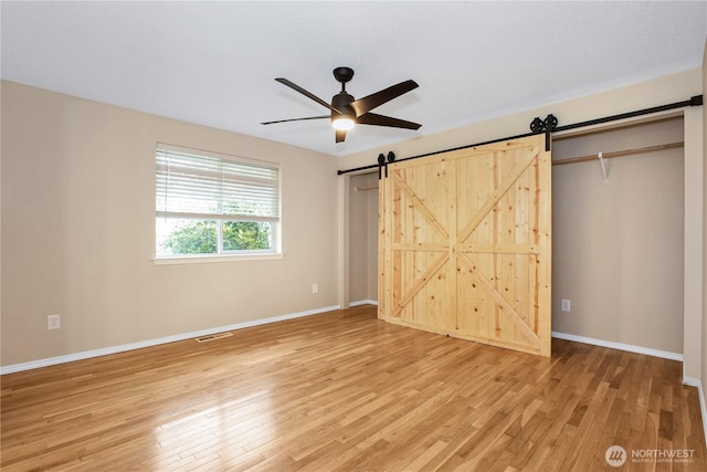 unfurnished bedroom with visible vents, light wood-style flooring, baseboards, and a barn door