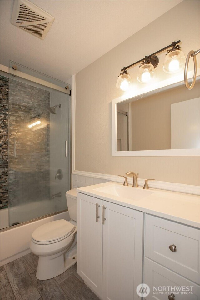 full bath featuring vanity, wood finished floors, visible vents, shower / bath combination with glass door, and toilet