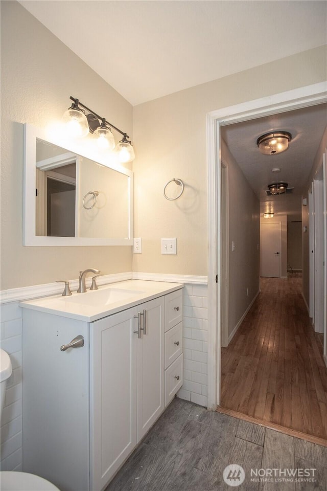 half bath featuring vanity, wood finished floors, wainscoting, tile walls, and toilet