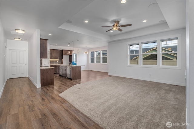 kitchen with baseboards, a tray ceiling, dark wood-style flooring, light countertops, and open floor plan