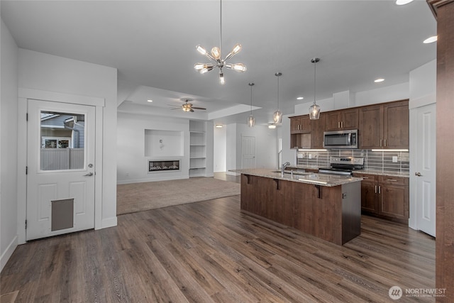 kitchen with open floor plan, dark wood-style floors, a glass covered fireplace, stainless steel appliances, and a sink