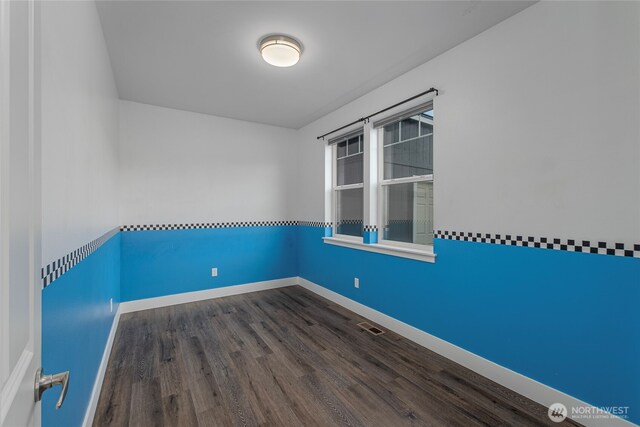 unfurnished room featuring dark wood-type flooring, visible vents, and baseboards