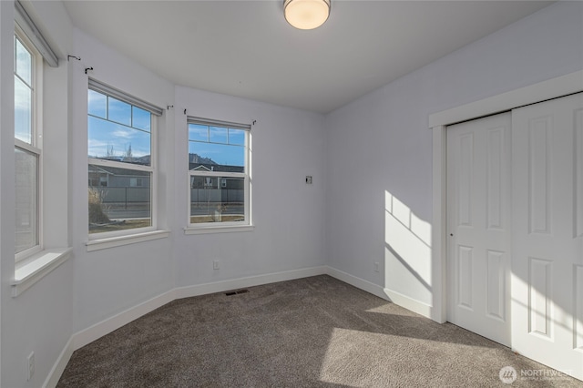 unfurnished bedroom with a closet, baseboards, visible vents, and dark carpet