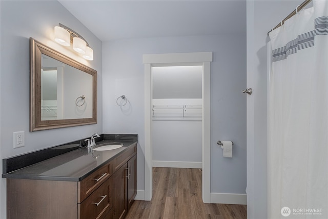 bathroom featuring vanity, a spacious closet, wood finished floors, and baseboards