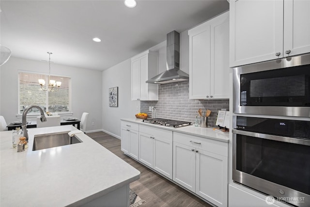 kitchen featuring dark wood-style flooring, stainless steel appliances, a sink, light countertops, and wall chimney exhaust hood