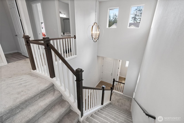 staircase with a notable chandelier, carpet flooring, baseboards, and wood finished floors