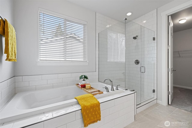 full bathroom with a walk in closet, a shower stall, a bath, and baseboards