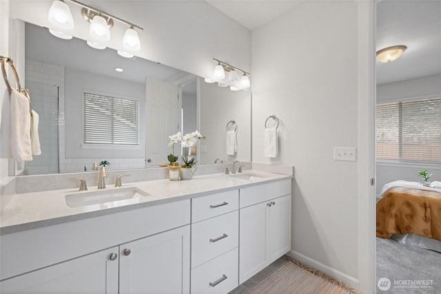 ensuite bathroom with a sink, baseboards, ensuite bath, and double vanity