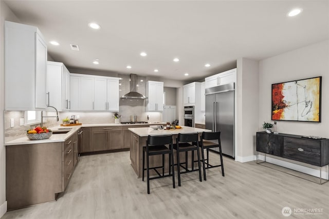 kitchen with a kitchen island, a kitchen bar, stainless steel appliances, wall chimney exhaust hood, and a sink