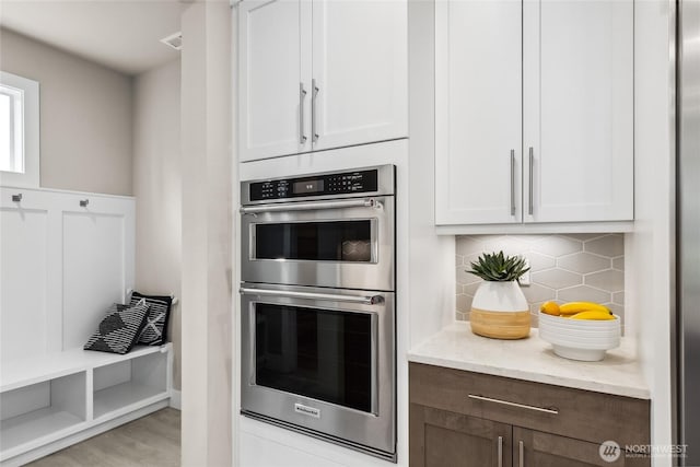 kitchen with white cabinets, light stone countertops, tasteful backsplash, and stainless steel double oven