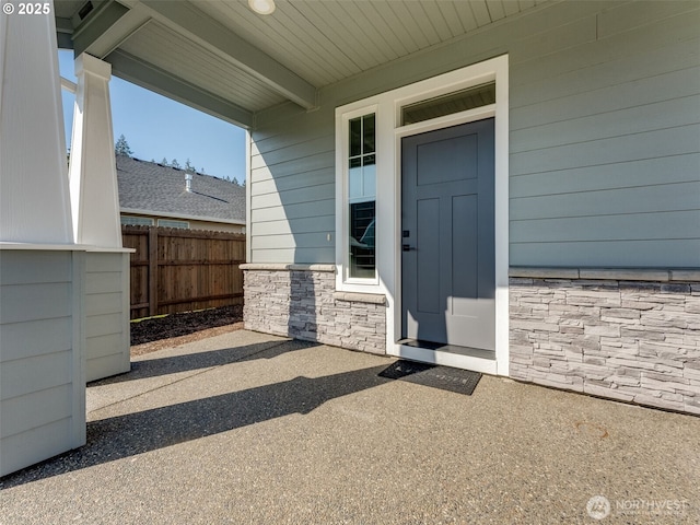 entrance to property featuring stone siding and fence