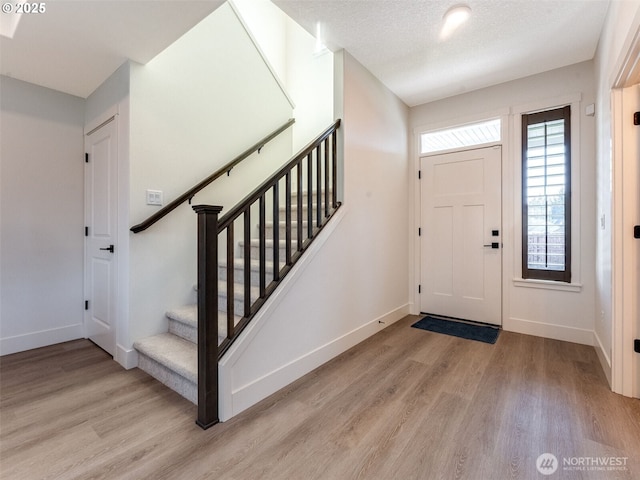 foyer entrance featuring stairway, baseboards, a textured ceiling, and wood finished floors