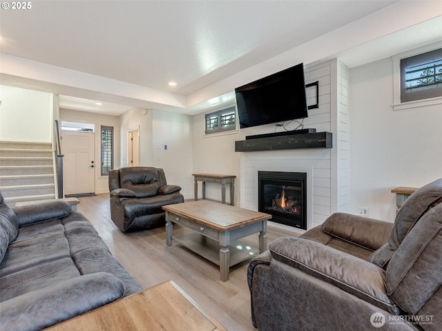 living area with a large fireplace, stairs, a wall unit AC, recessed lighting, and wood finished floors