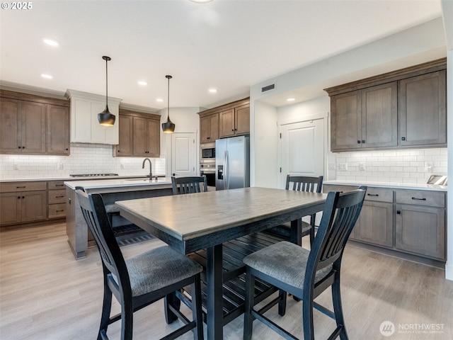 kitchen featuring visible vents, a kitchen island with sink, light wood-style floors, appliances with stainless steel finishes, and tasteful backsplash