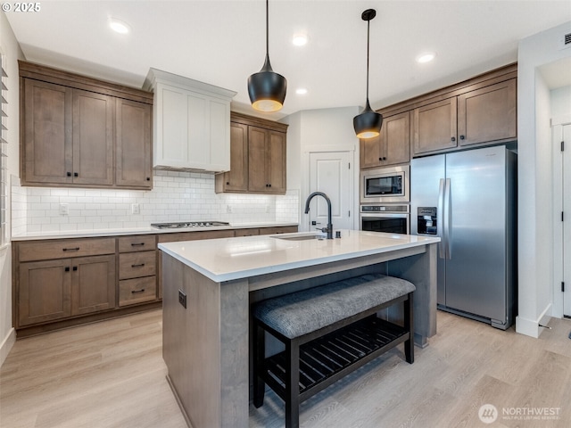 kitchen featuring a sink, decorative backsplash, light wood-style floors, appliances with stainless steel finishes, and a kitchen bar