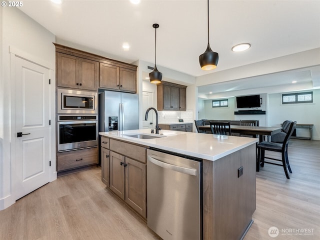 kitchen featuring a sink, stainless steel appliances, a center island with sink, and light wood-style flooring