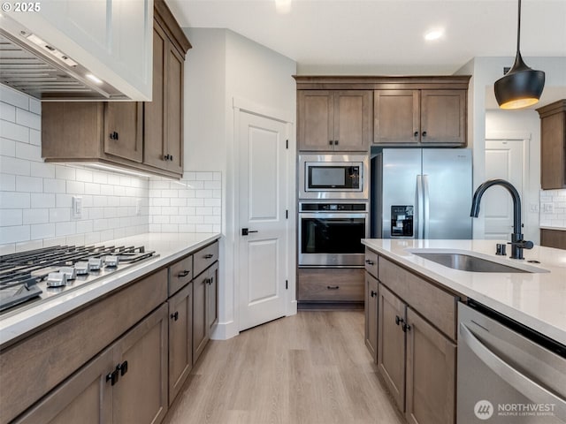 kitchen featuring a sink, ventilation hood, appliances with stainless steel finishes, light wood finished floors, and decorative backsplash