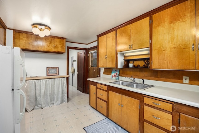 kitchen featuring brown cabinets, a sink, freestanding refrigerator, light countertops, and light floors