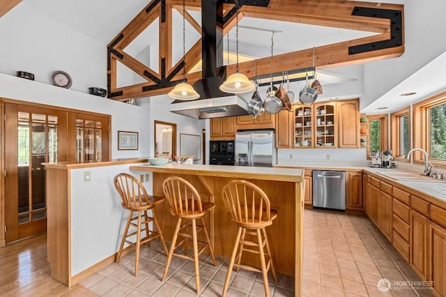 kitchen featuring a sink, a kitchen breakfast bar, tile countertops, stainless steel appliances, and glass insert cabinets