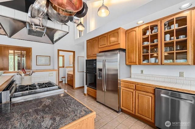 kitchen featuring light tile patterned floors, brown cabinets, appliances with stainless steel finishes, and glass insert cabinets