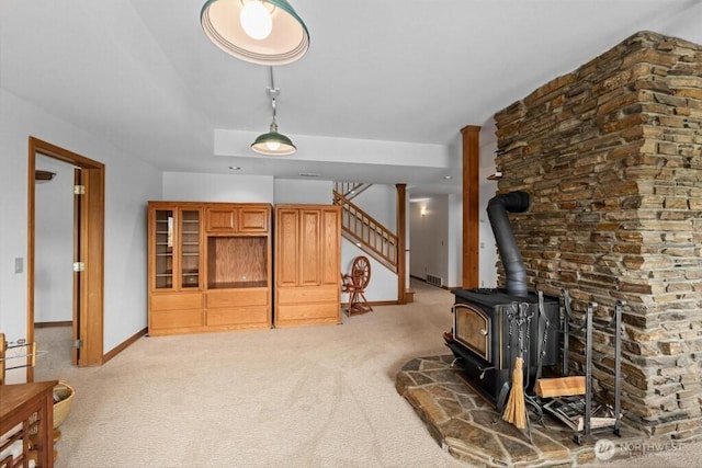 living area with visible vents, baseboards, stairway, light carpet, and a wood stove