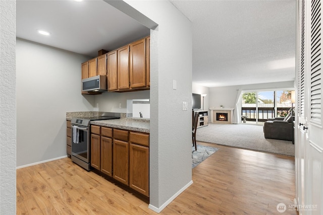 kitchen featuring light wood-type flooring, a lit fireplace, stainless steel appliances, open floor plan, and brown cabinets