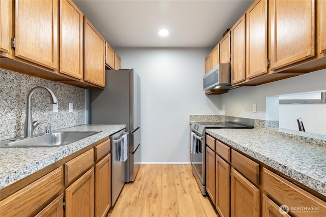 kitchen featuring a sink, light countertops, appliances with stainless steel finishes, tasteful backsplash, and light wood-type flooring