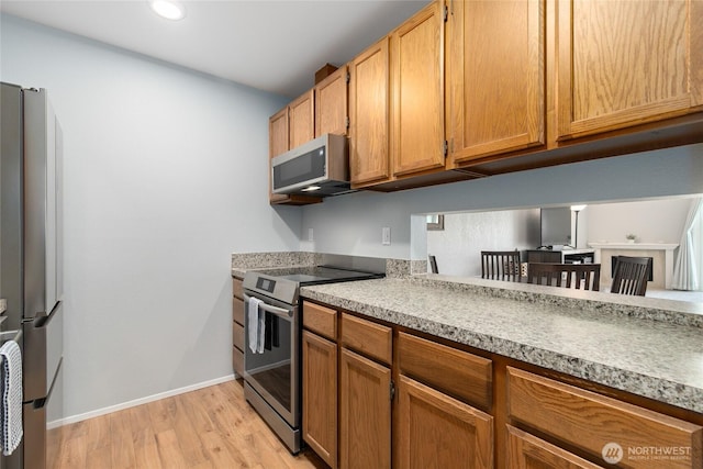 kitchen featuring light wood-type flooring, brown cabinets, appliances with stainless steel finishes, light countertops, and baseboards