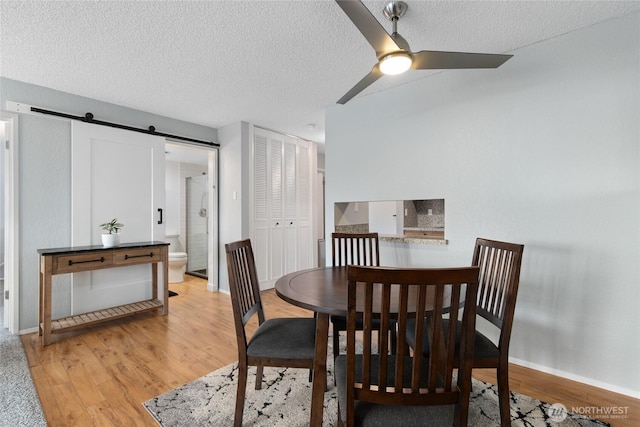 dining space with a barn door, light wood-style flooring, a ceiling fan, and a textured ceiling