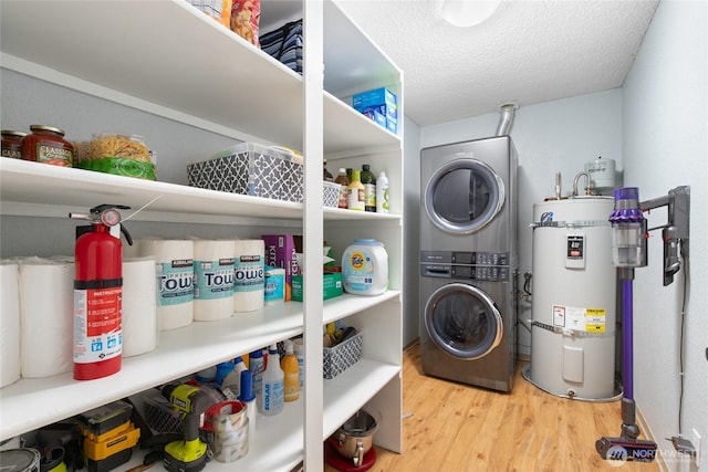 washroom with wood finished floors, secured water heater, laundry area, stacked washer and clothes dryer, and a textured ceiling